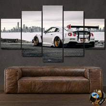 Load image into Gallery viewer, Multi-panel canvas print of a white Nissan GT-R R35 Liberty Walk with city skyline background, displayed above a brown leather sofa