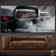 Load image into Gallery viewer, Three-piece canvas wall art featuring rear view of smoky Pontiac Firebird Trans Am sports cars above brown leather sofa