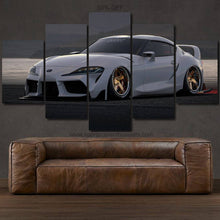 Load image into Gallery viewer, Multi-panel canvas wall art featuring a white Toyota Supra MK5 sports car displayed above a brown leather sofa