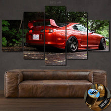 Load image into Gallery viewer, Multi-panel canvas wall art featuring a red Toyota Supra MK4 sports car in a forest setting above a brown leather sofa