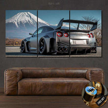 Load image into Gallery viewer, Three-piece framed canvas of a black GTR Liberty Walk car with Mount Fuji in the background displayed above a brown leather sofa